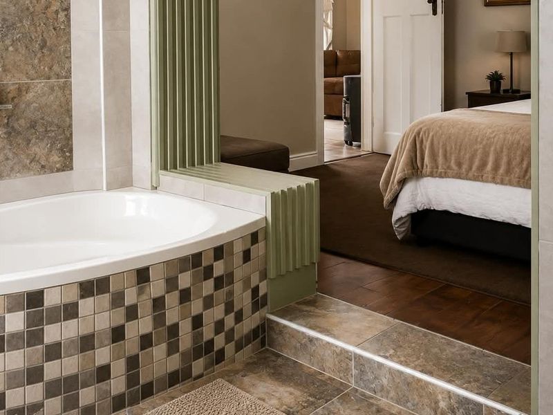 A well-maintained bathroom featuring a built-in bathtub with mosaic tile detailing, stone-look floor tiles, and a decorative timber slat partition.