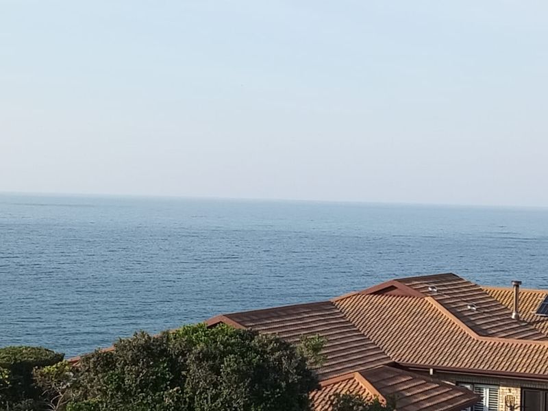 A scenic elevated view of the ocean featuring a residential property with a tiled roof and installed solar panels.