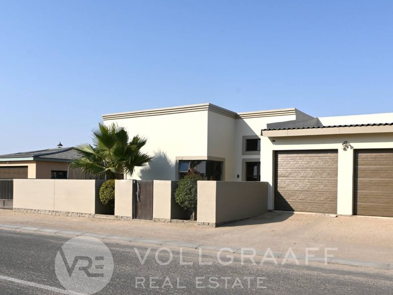 Front exterior view of a modern house featuring a double garage with roller shutter doors and a secure boundary wall with a pedestrian gate.