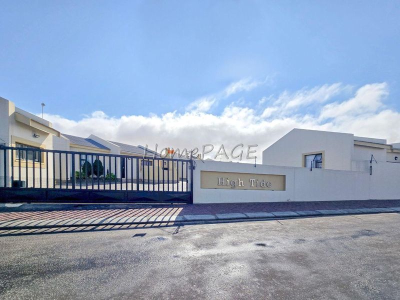 Front exterior view of the High Tide townhouse complex featuring a secure gated entrance, perimeter walling, and paved driveway access.