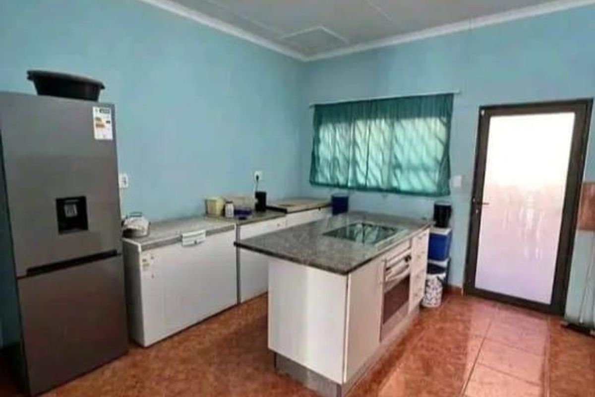 A functional kitchen space featuring a central island with a built-in hob and oven, tiled flooring, and direct access to an exterior door.