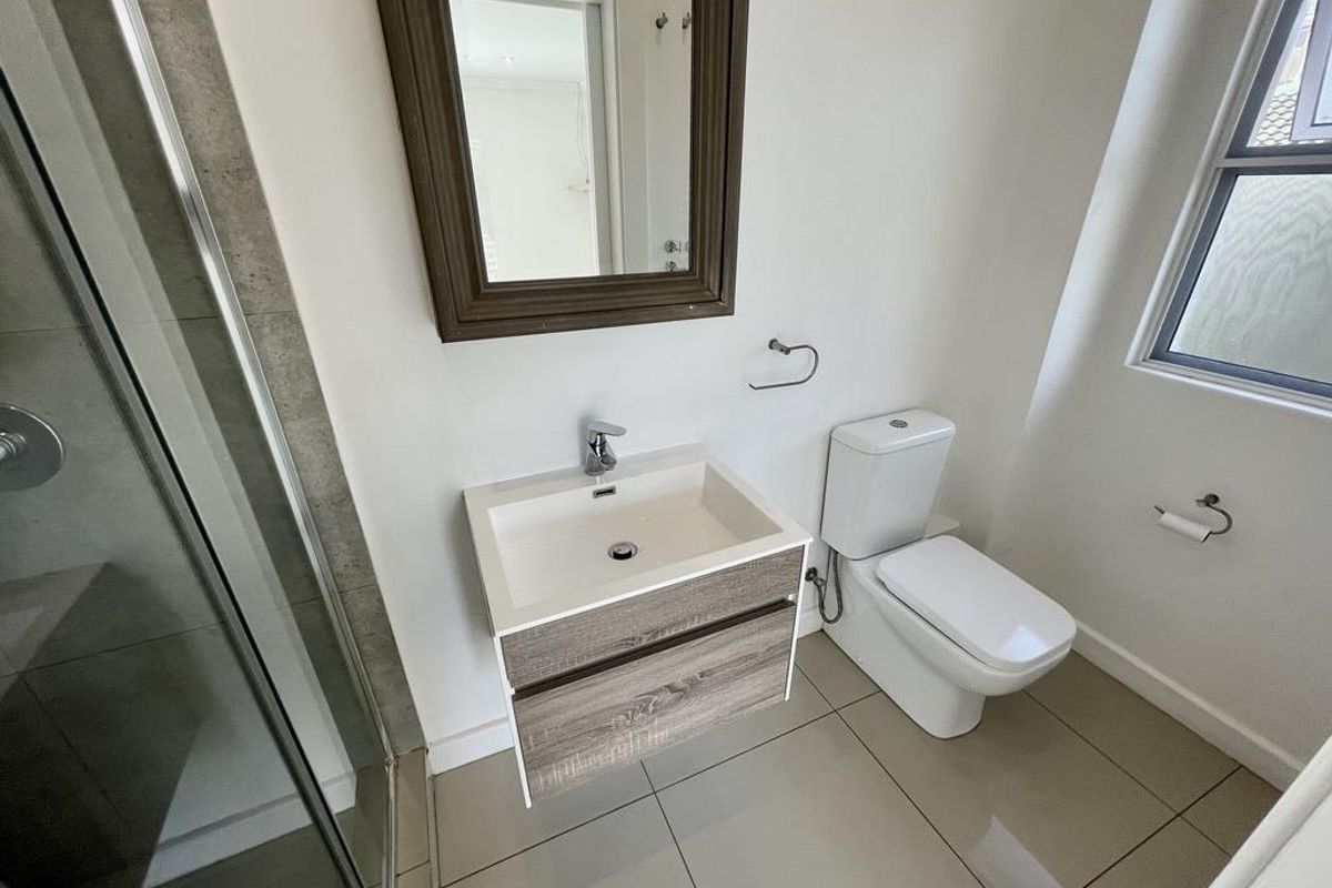 Modern bathroom featuring a vanity with basin, a toilet, and a glass-enclosed shower with neutral floor and wall tiling.