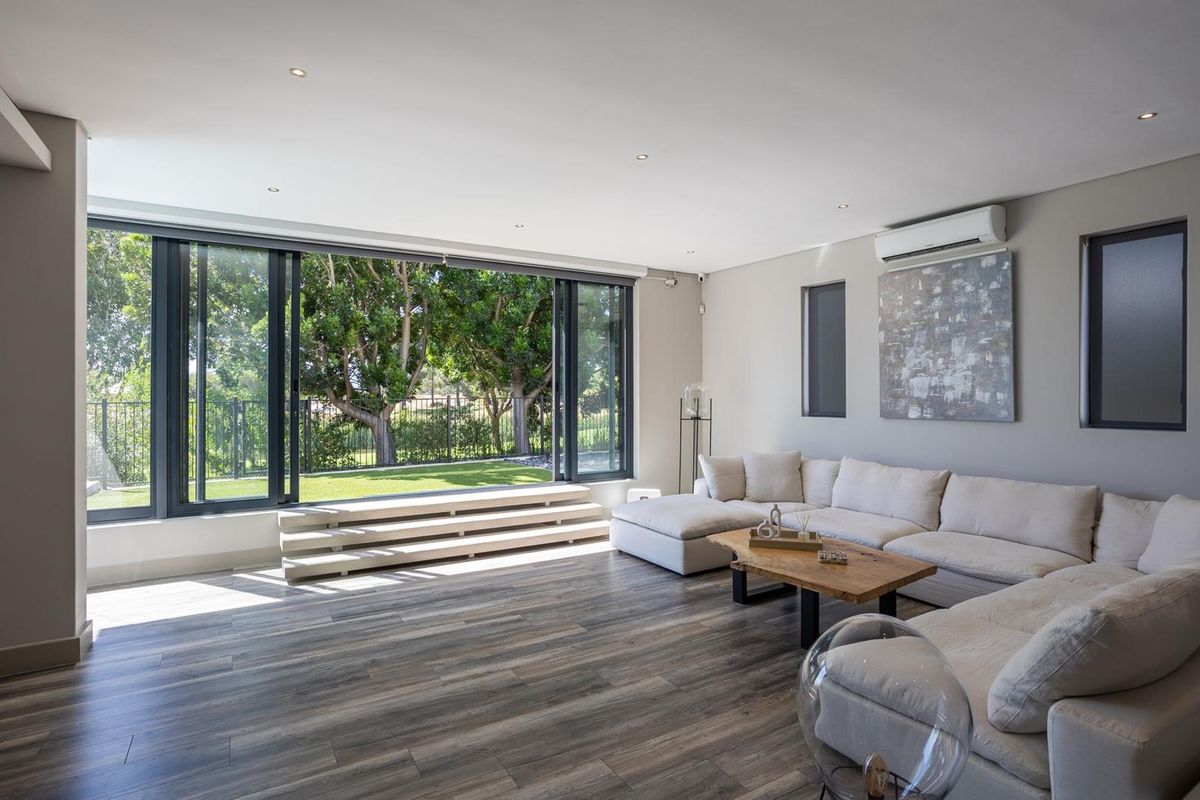 Spacious living room featuring modern timber-look flooring, recessed lighting, and large sliding glass doors that open to a private garden view.