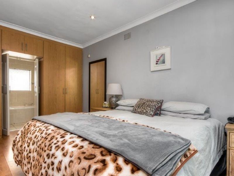 A bedroom featuring built-in wooden cupboards, laminate flooring, and direct access to an en-suite bathroom.