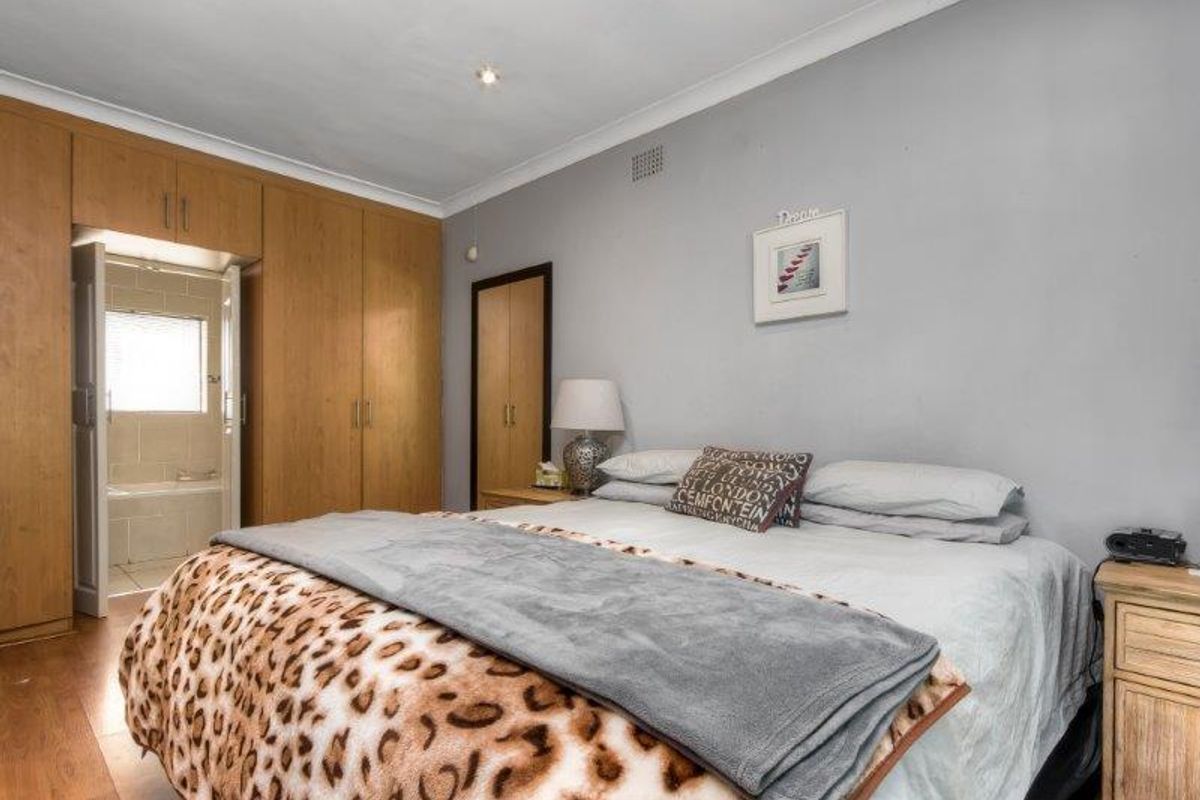 A bedroom featuring built-in wooden cupboards, laminate flooring, and direct access to an en-suite bathroom.