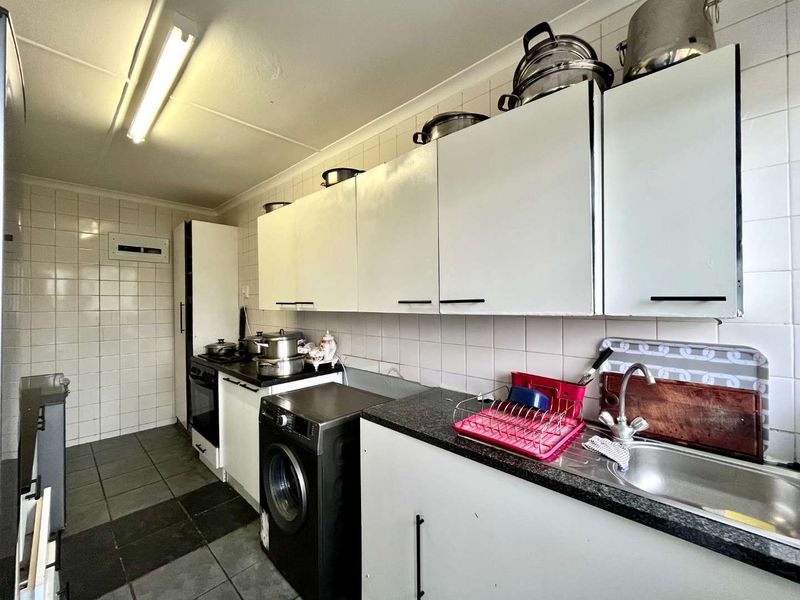 A functional kitchen featuring white cabinetry, dark laminate countertops, tiled backsplash, and tiled flooring, providing a practical workspace with integrated oven and sink.