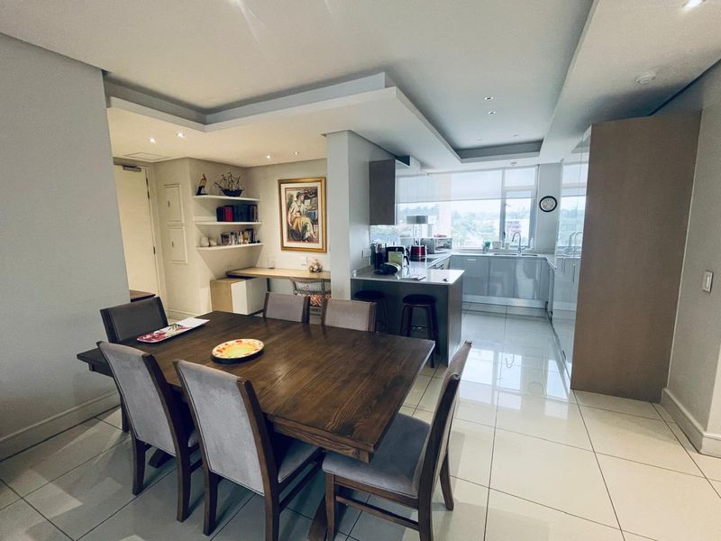 Modern open-plan living and dining area featuring a sleek kitchen with island, built-in cabinetry, and bright, tiled flooring throughout.