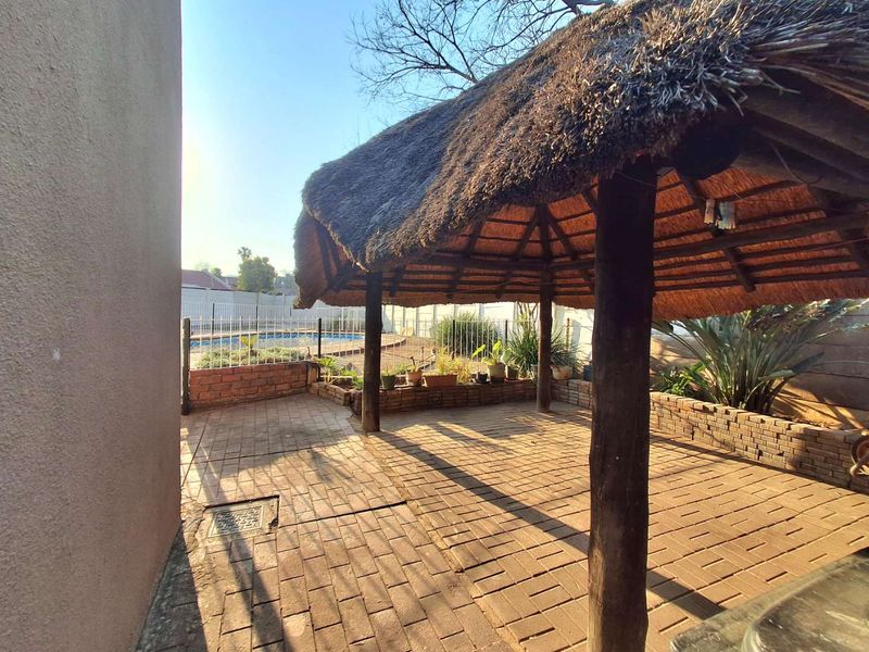 Outdoor entertainment area featuring a traditional thatched lapa, brick paving, and a built-in brick retaining wall overlooking the swimming pool.