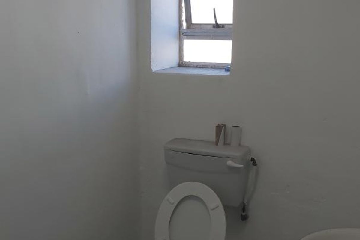 A basic industrial restroom featuring a standard toilet, wall-mounted cistern, and a small basin with a window for natural ventilation.