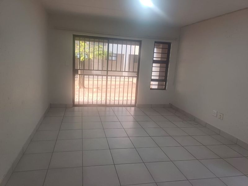 An empty, neutrally painted living area featuring tiled flooring, a sliding glass door with security gate, and natural light access.