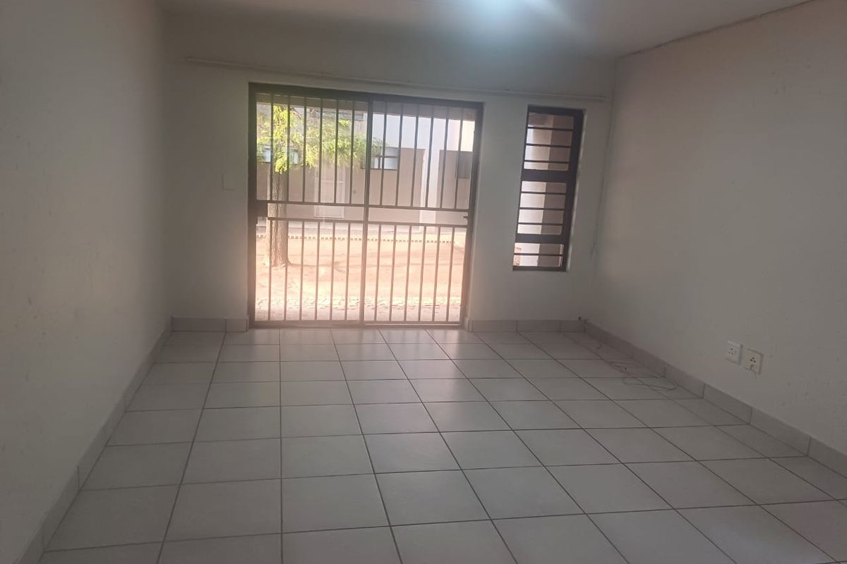 An empty, neutrally painted living area featuring tiled flooring, a sliding glass door with security gate, and natural light access.