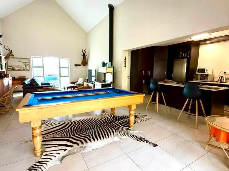 Spacious open-plan living area featuring a vaulted ceiling, tiled floors, a freestanding fireplace, and a functional kitchen with a breakfast island.