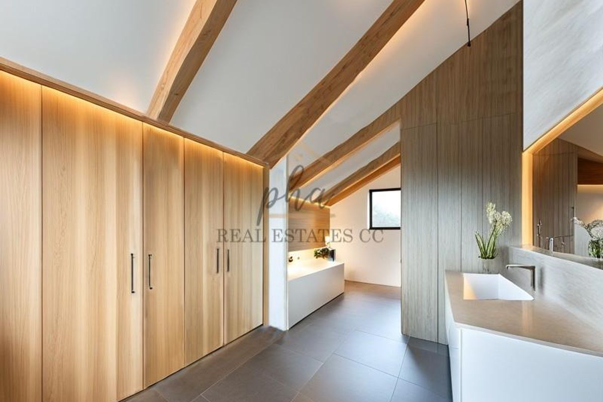 Modern attic-style bathroom featuring high-end timber cabinetry, exposed wooden beams, integrated LED lighting, a sleek vanity basin, and a built-in bathtub.