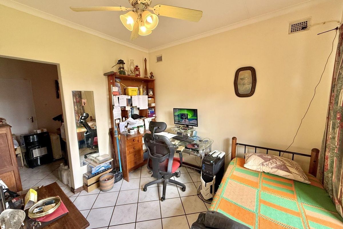 A functional bedroom featuring tiled flooring, a ceiling fan, and built-in ventilation, currently utilized as a multi-purpose workspace.