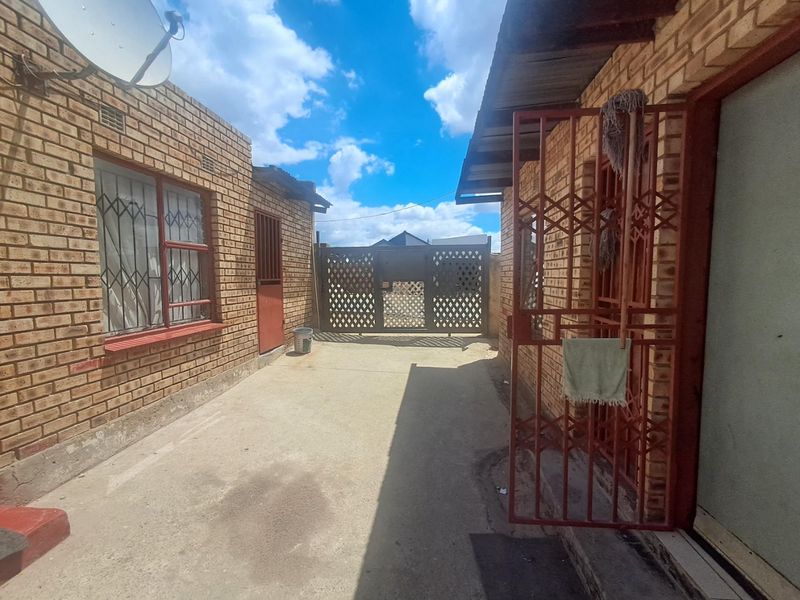 A view of the rear exterior area featuring face brick walls, security gates, and a concrete driveway leading to a metal gate.
