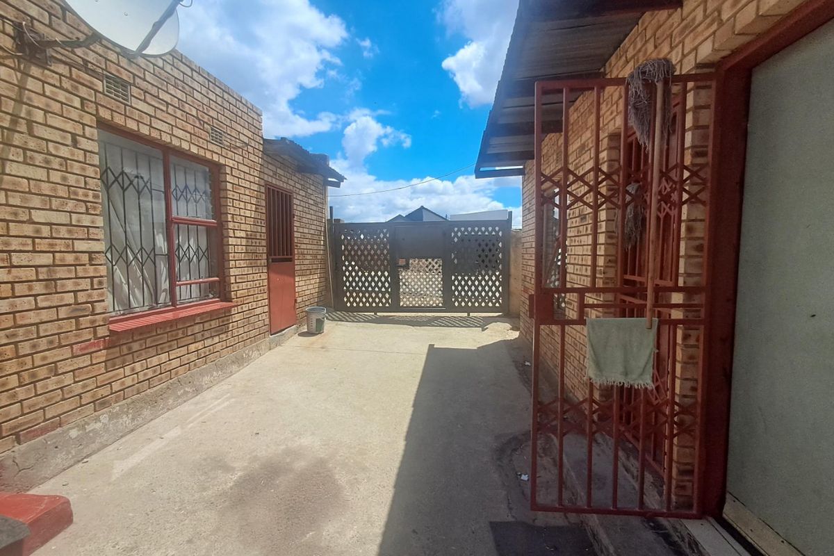 A view of the rear exterior area featuring face brick walls, security gates, and a concrete driveway leading to a metal gate.