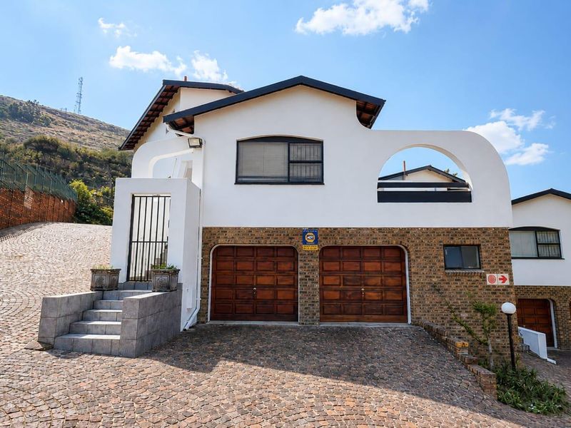 Front elevation of a townhouse featuring a double wooden garage, cobblestone driveway, and distinctive arched architectural detailing.