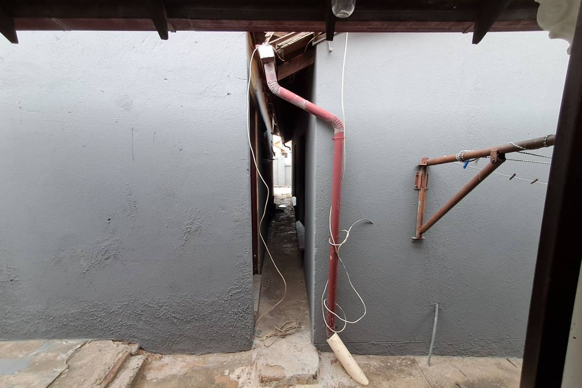 A narrow exterior side passage showing significant maintenance requirements, including damaged roof eaves, exposed wiring, and a broken downpipe system.