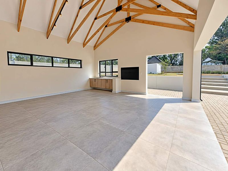 Spacious open-plan living area featuring high vaulted ceilings with exposed timber trusses, tiled floors, built-in cabinetry with sink, and a fireplace, opening to a patio.