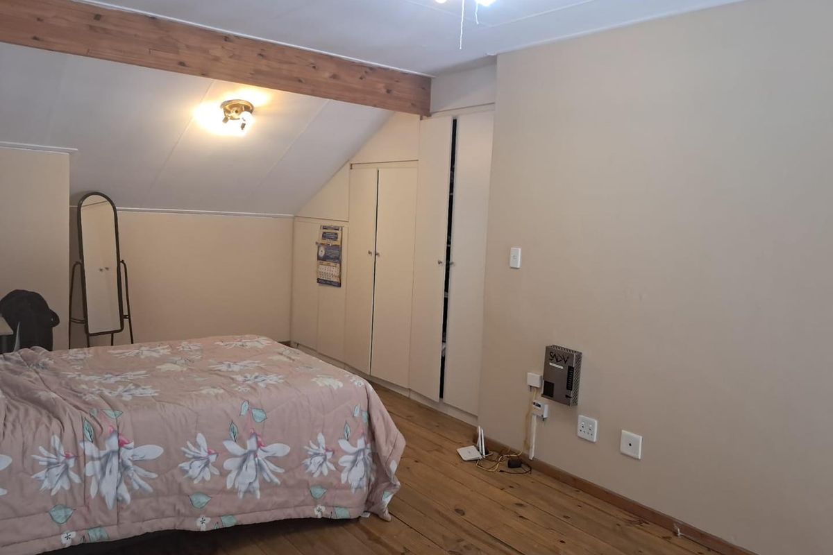 Bedroom featuring timber flooring, exposed wooden ceiling beam, sloped ceiling, and built-in storage cupboards.