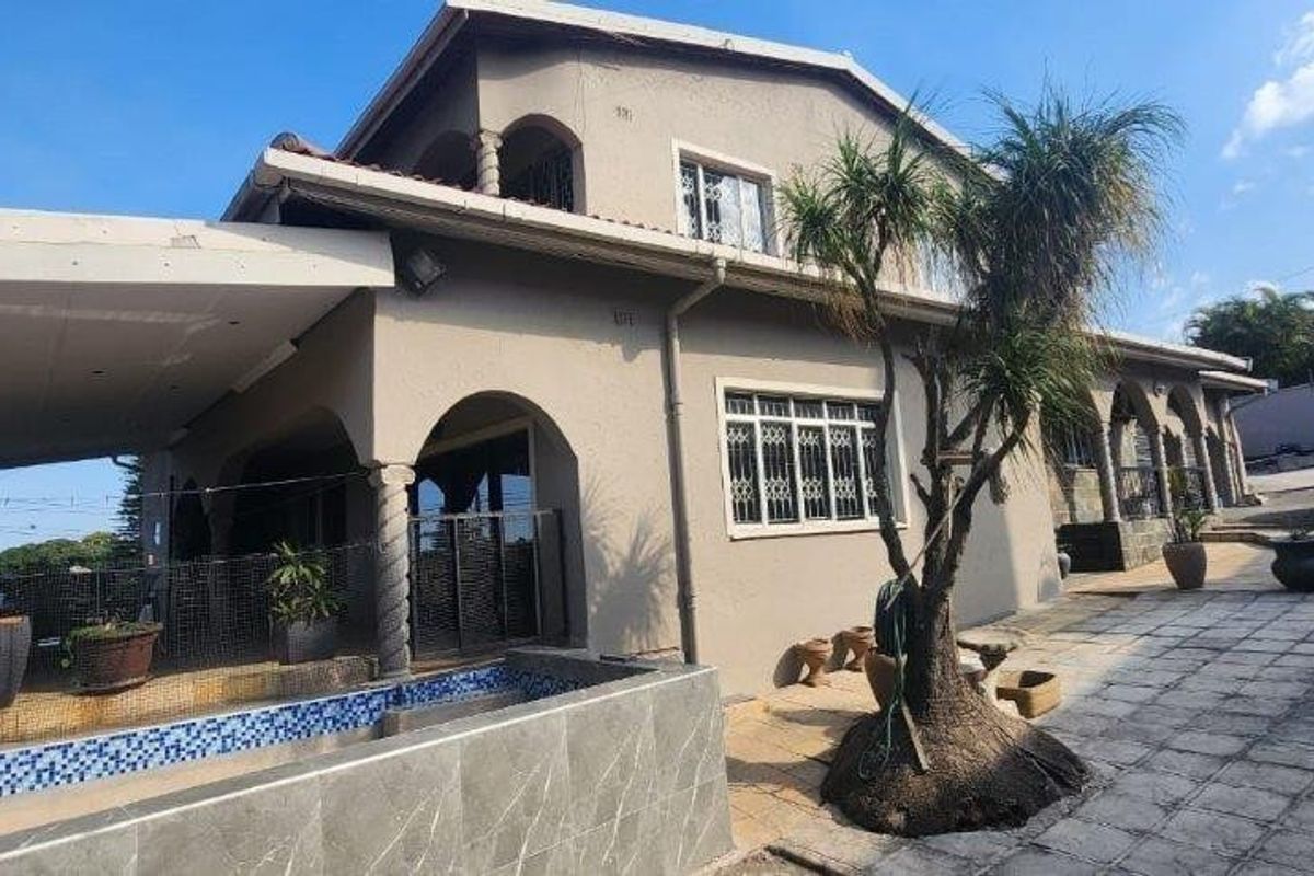 Rear exterior view of the house featuring a covered patio, tiled swimming pool, and paved outdoor area.