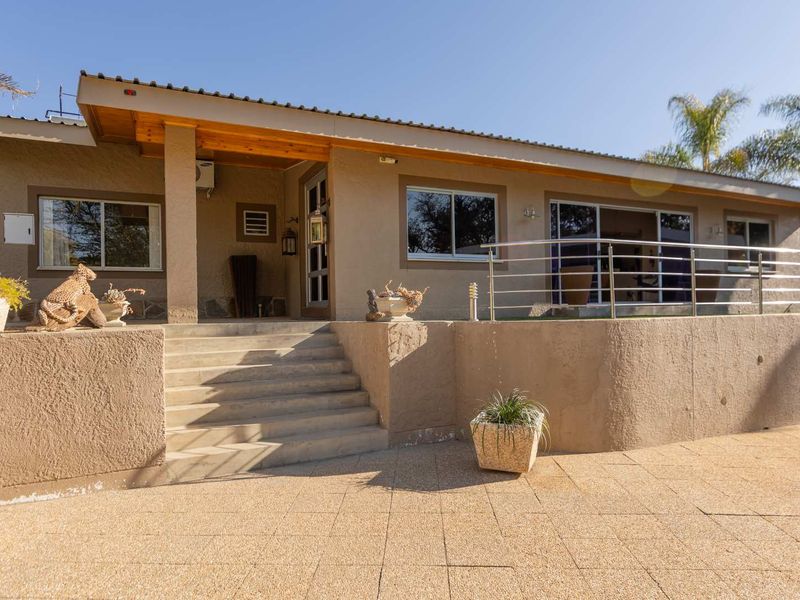 Front elevation featuring a raised patio with stainless steel balustrades, concrete stairs, and sliding glass doors leading into the home.