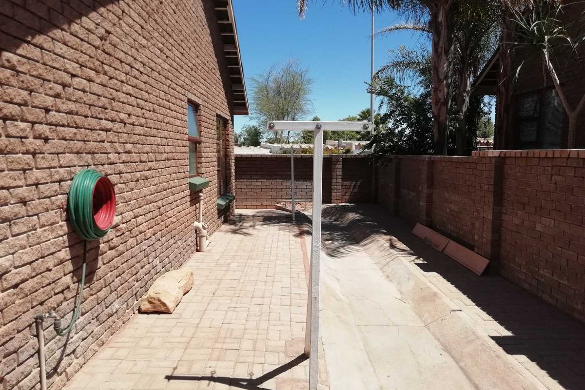 A side exterior area featuring brick walls, paved flooring, and a fixed metal washing line structure with an integrated concrete drainage channel.