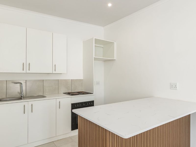 A clean, modern kitchen featuring white cabinetry, a stone-look countertop, built-in oven and hob, and a tiled backsplash.