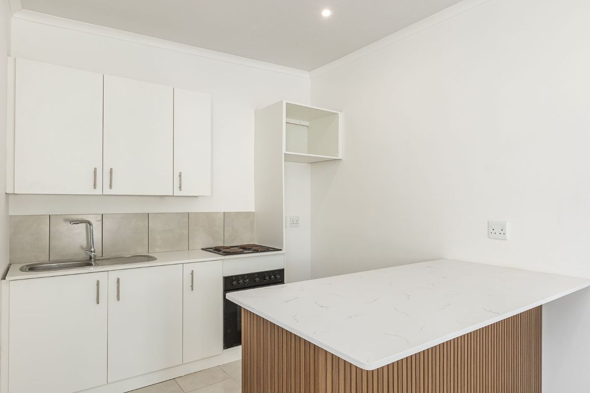 A clean, modern kitchen featuring white cabinetry, a stone-look countertop, built-in oven and hob, and a tiled backsplash.