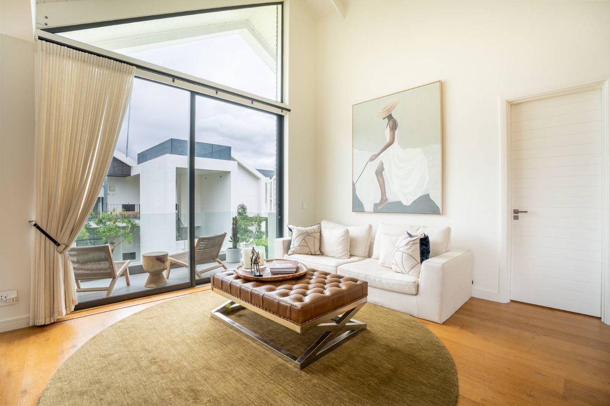 Bright living room featuring high vaulted ceilings, hardwood flooring, and large sliding glass doors that open onto a private balcony.