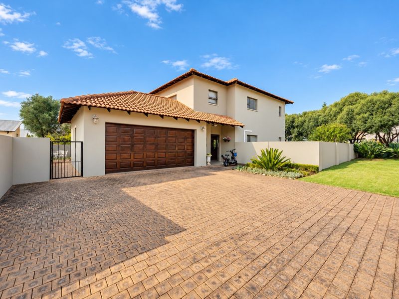 A well-maintained double-story house featuring a paved driveway, a double garage with wooden doors, and a neat front garden with boundary walls.