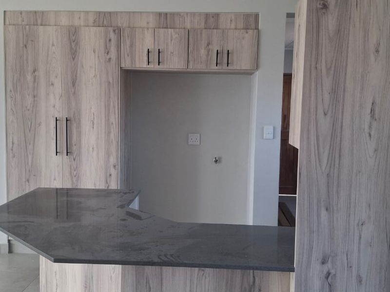 A modern kitchen featuring light wood-grain cabinetry, a dark stone breakfast bar, and neutral tiled flooring in an open-plan layout.