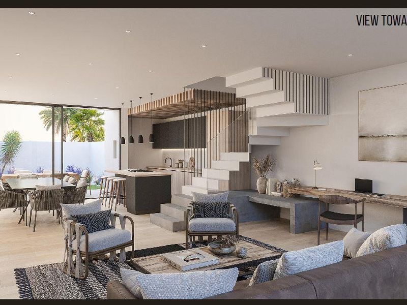 Modern open-plan living area featuring a sleek kitchen, integrated staircase, built-in desk, and seamless flow to the outdoor patio and garden.