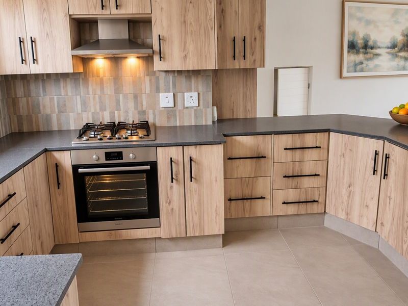 Modern kitchen featuring light wood-grain cabinetry, dark stone countertops, a gas hob, built-in oven, and a stylish tiled backsplash.