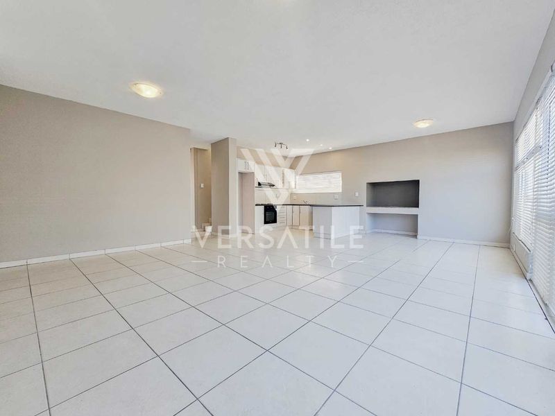 Spacious open-plan living area featuring tiled flooring, a modern kitchen with built-in appliances, and a built-in fireplace, offering a bright and versatile layout.