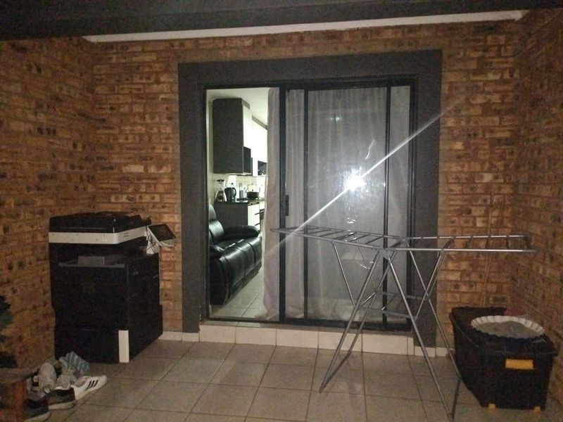 A covered patio area featuring exposed brick walls and tiled flooring, providing access to the interior living space through a sliding glass door.
