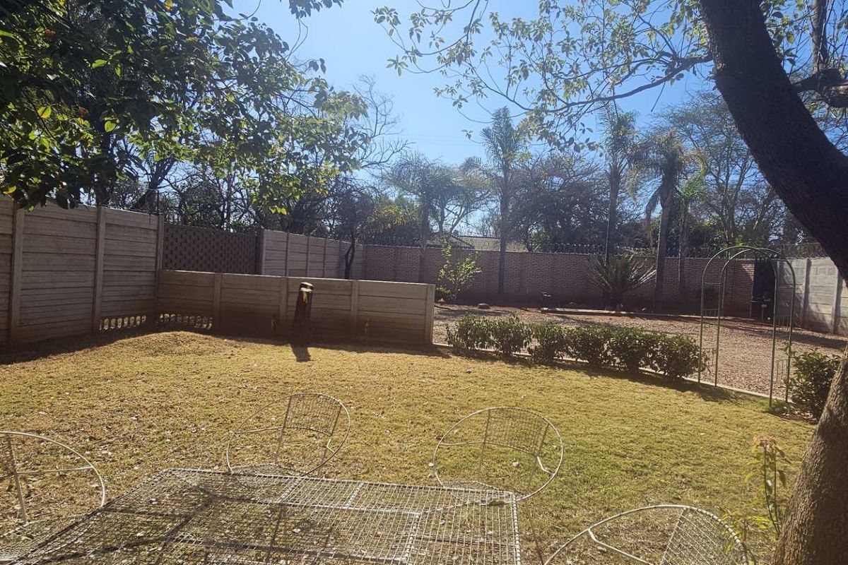A spacious, level garden area featuring established trees, a well-maintained lawn, and secure perimeter boundary walls.