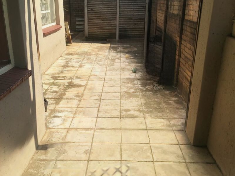 A narrow rear exterior area featuring tiled paving, a brick boundary wall, and a corrugated metal storage shed.