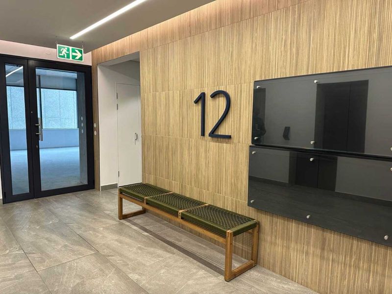 Modern office lobby or corridor featuring wood veneer wall paneling, large format porcelain floor tiles, and integrated linear lighting.