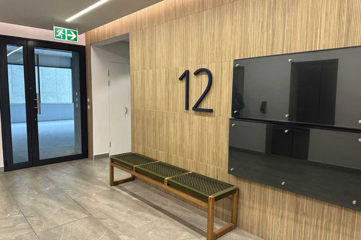 Modern office lobby or corridor featuring wood veneer wall paneling, large format porcelain floor tiles, and integrated linear lighting.