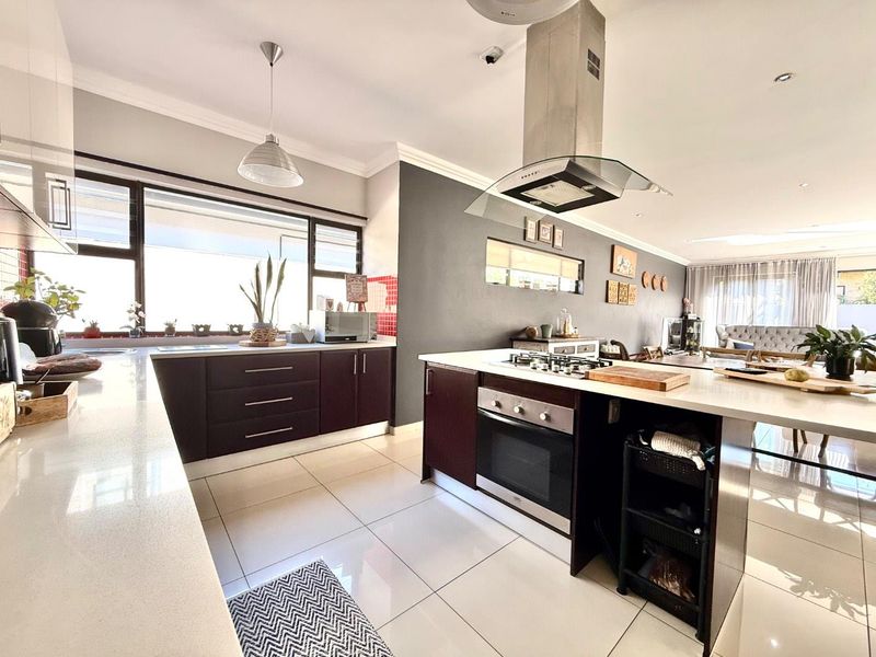 Modern open-plan kitchen featuring a central island with built-in oven and gas hob, stone countertops, and sleek dark cabinetry, flowing into the living area.
