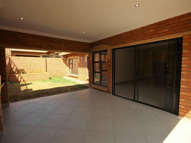 Covered patio featuring tiled flooring, a built-in braai, and sliding glass doors leading to a private garden area.