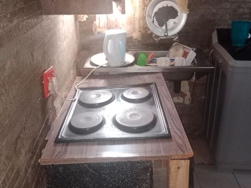 A compact kitchen area featuring a built-in electric hob, stainless steel sink, and tiled wall finishes, requiring cosmetic updates to improve functionality and aesthetic appeal.