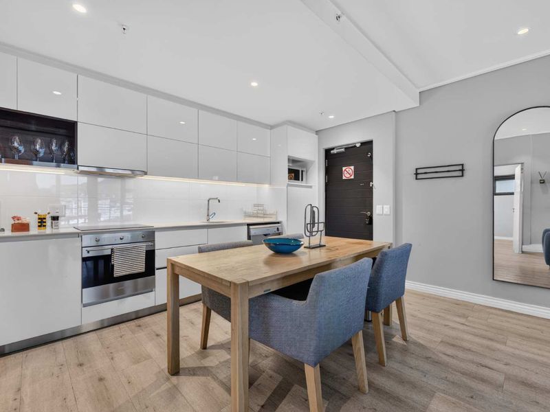 Modern open-plan kitchen featuring sleek white cabinetry, integrated appliances, and durable laminate flooring, seamlessly flowing into the dining area.