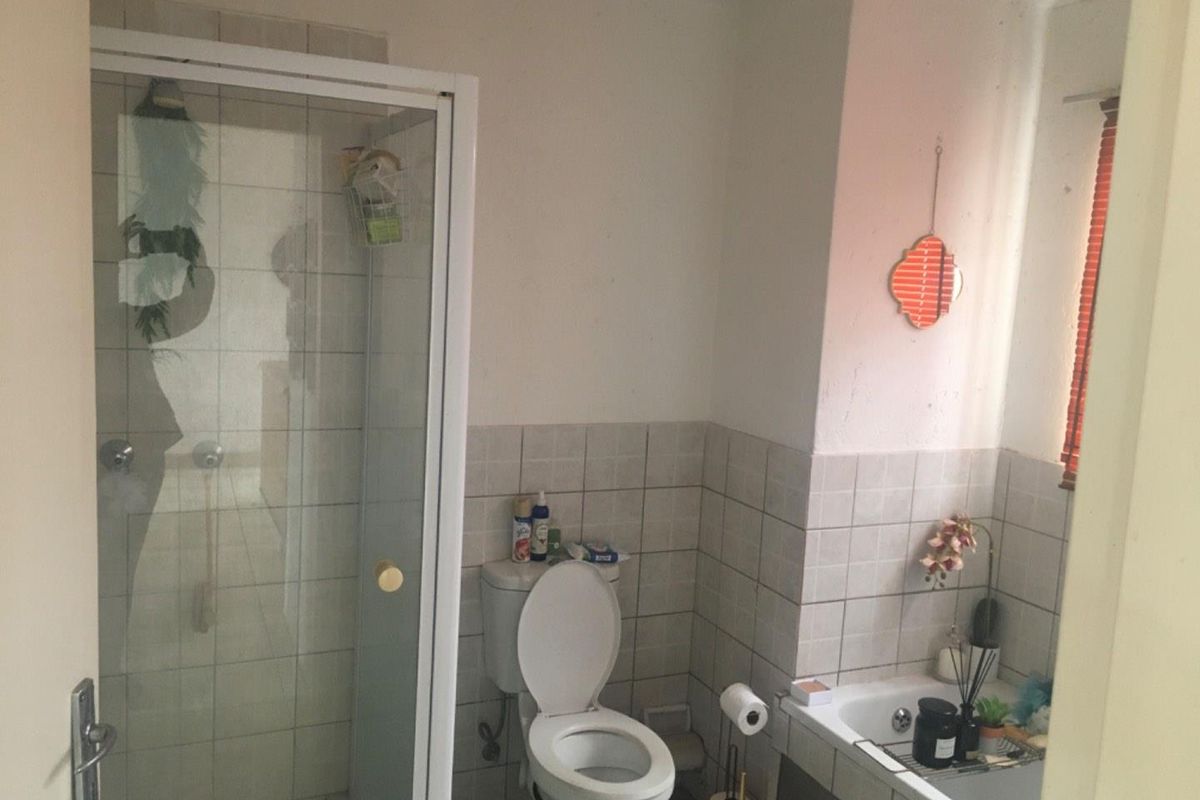A functional bathroom featuring a glass-enclosed shower, a standard toilet, and a tiled bathtub area with neutral wall tiling.