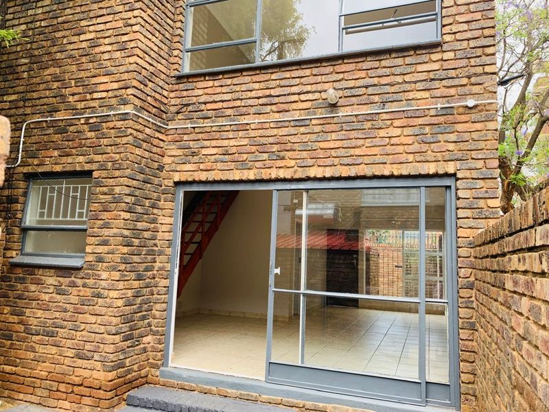 Rear view of an apartment featuring exposed brickwork, a sliding glass door entrance, and tiled flooring visible through the opening.