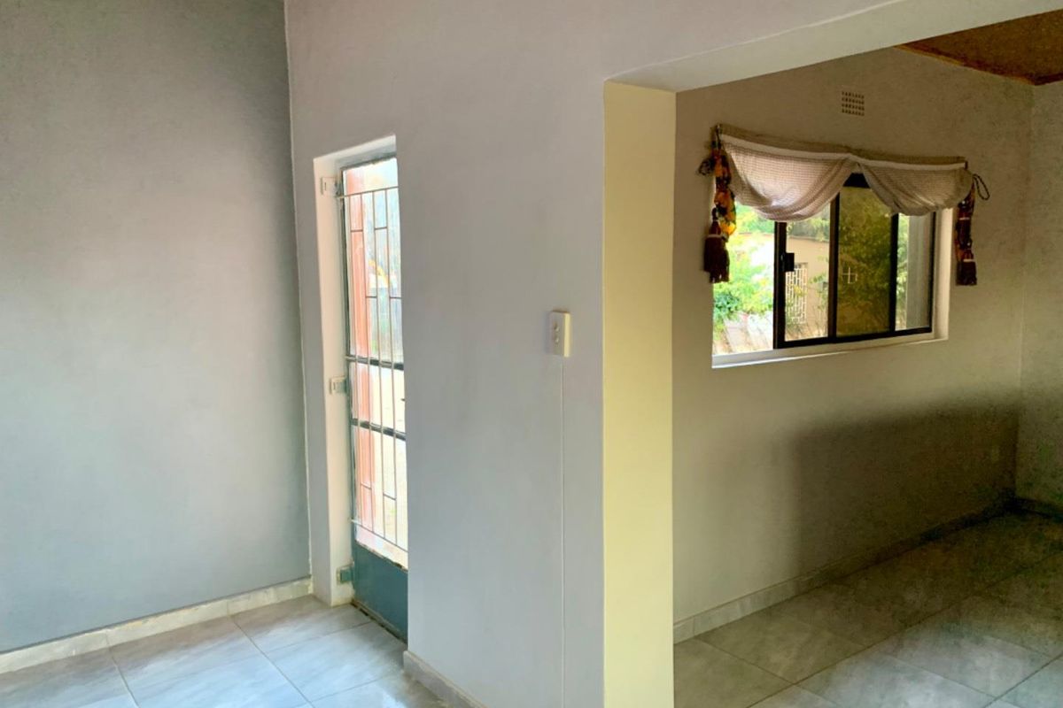 An interior view of a living area featuring tiled flooring, a security gate at the entrance, and a window with natural light.