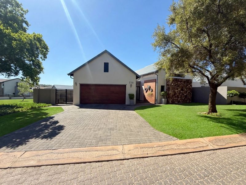 A well-maintained front elevation featuring a paved driveway, double garage with timber door, and attractive stone and brick architectural detailing.