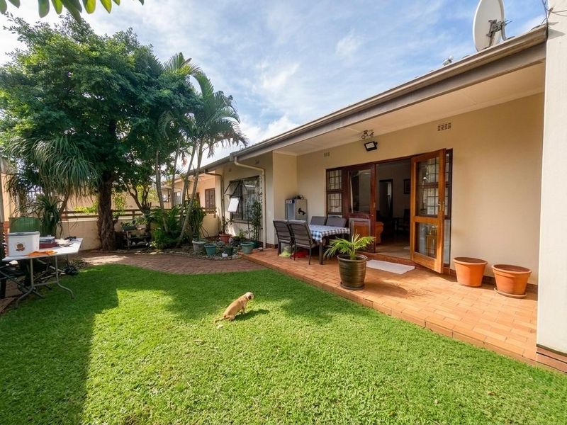 A rear view of the townhouse featuring a paved patio area, a well-maintained lawn, and direct access to the interior living space.