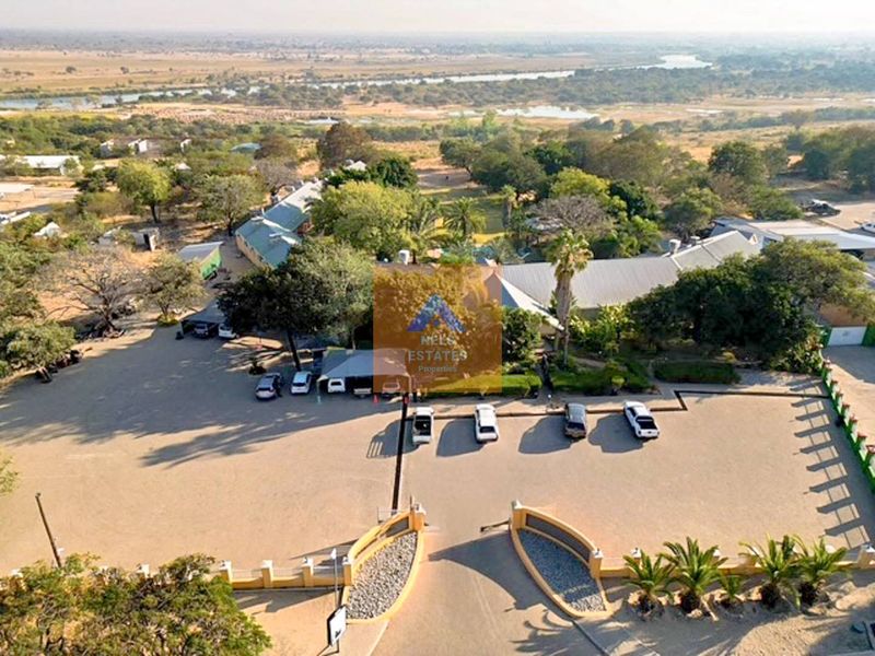 Aerial view of the hotel property featuring a gated entrance, extensive parking facilities, and surrounding landscaped grounds with metal-roofed structures.